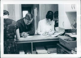 Students Ernie Klassen and Marina Reimer paying their fees; Gert Giesbrecht on left