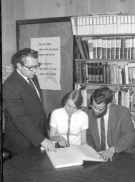 Frank H. Epp, standing looks at a book with Jon & Laurenda Messer