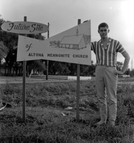 Gerald Loewen is standing by the sign for the future Altona Mennonite Church (Altona, Manitoba)