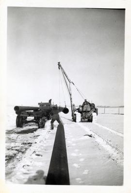 Three men with a side boom cat (tractor equipped with lifting boom) lifting pipeline off a truck
