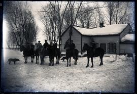 Outdoor group of 6 mounted horsemen in front of house.