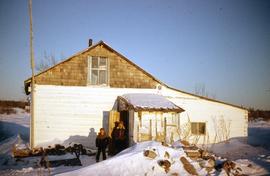 Two children standing in front of a snow covered house in Bloodvein First Nation, Manitoba