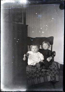 Interior portrait of two young children on a chair.