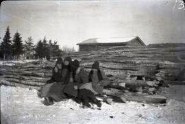 Four girls sitting at the base of a log pile