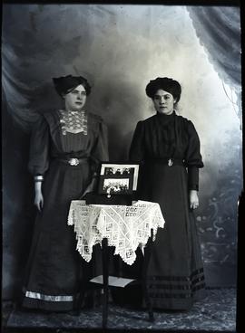 Two women with a table and two photos.