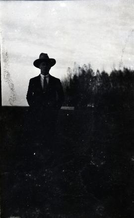 Under-exposed shot of man with hat standing outside.