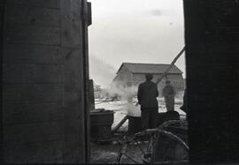 Two men burning something in a barrel in a farmyard