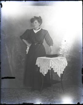 Woman standing before photo backdrop and lace covered table.